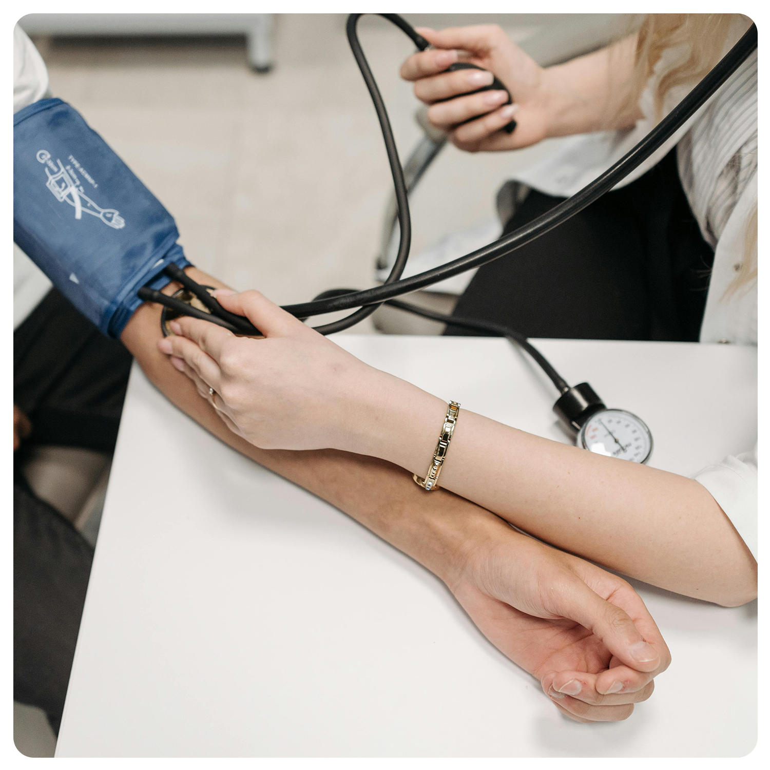 Eine medizinische Fachkraft führt gesundheitschecks kassel durch und misst den Blutdruck einer Person mit einer blauen Manschette und einem manuellen Blutdruckmessgerät, wobei beide Hände auf einem weißen Tisch sichtbar sind.